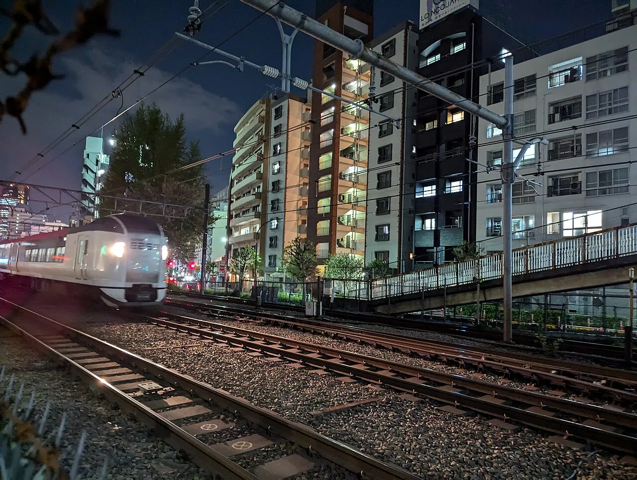 A white and red Narita Express train passing apartment blocks in Tokyo at night