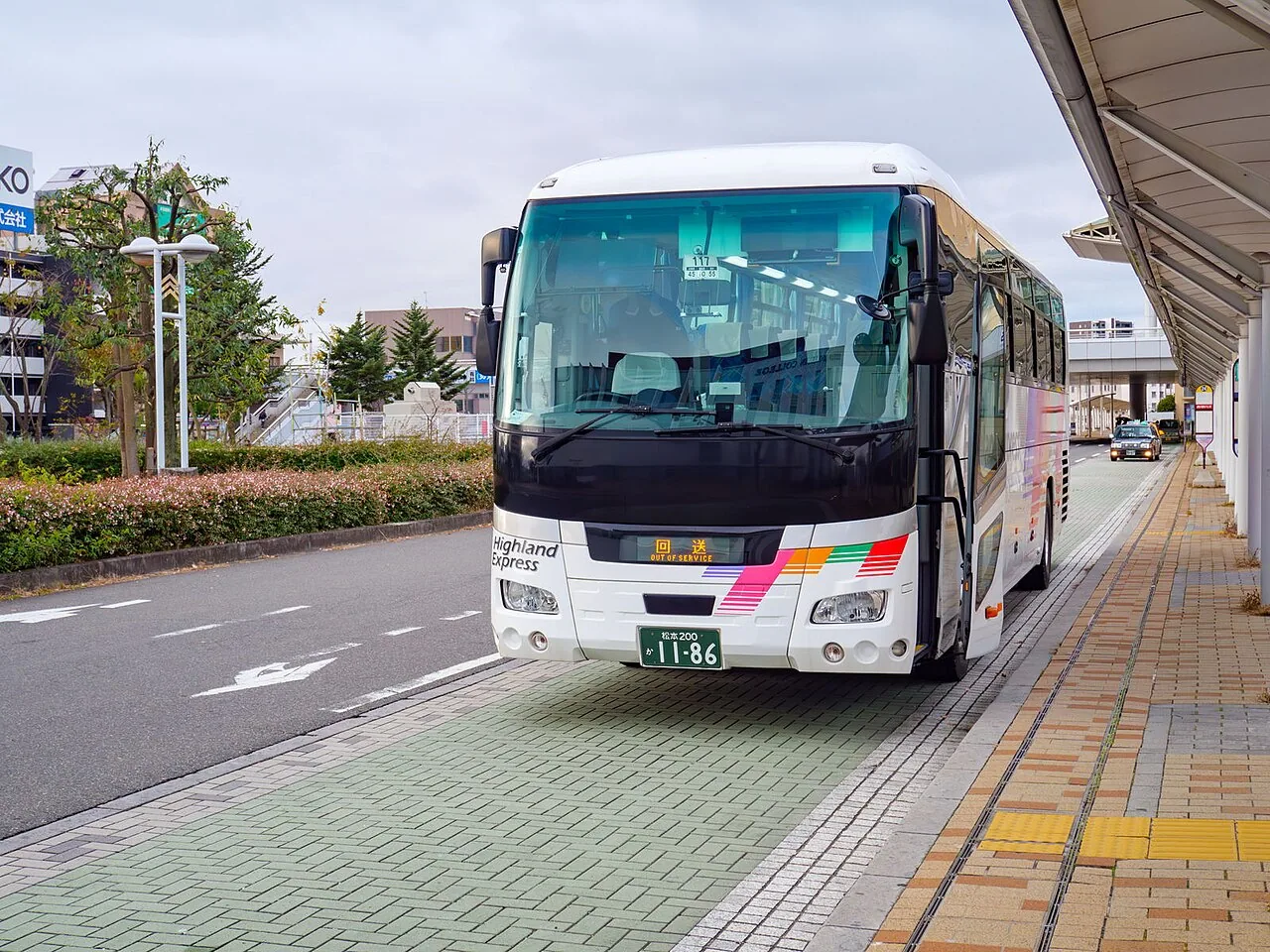 A white Alpico express coach parked at a covered bus stop at Nagano Station's east exit