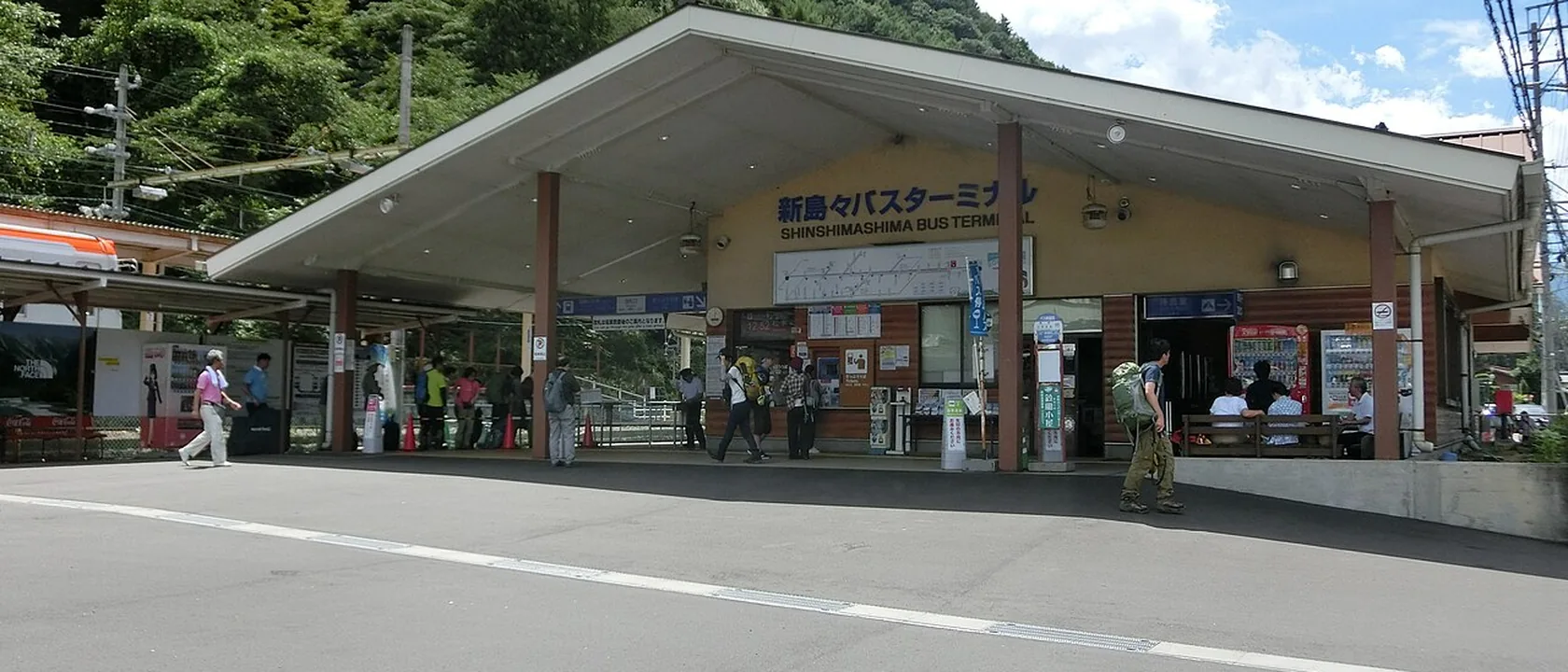 Shin-Shimashima bus terminal, a low building under a wide roof, with hikers carrying backpacks in front
