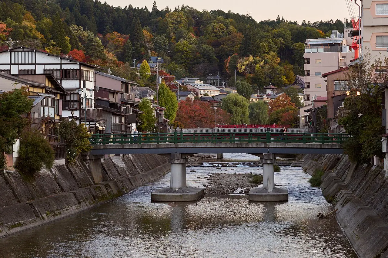 The Miyagawa River running through Takayama, with a bridge, houses and autumn colors on the hillside in November