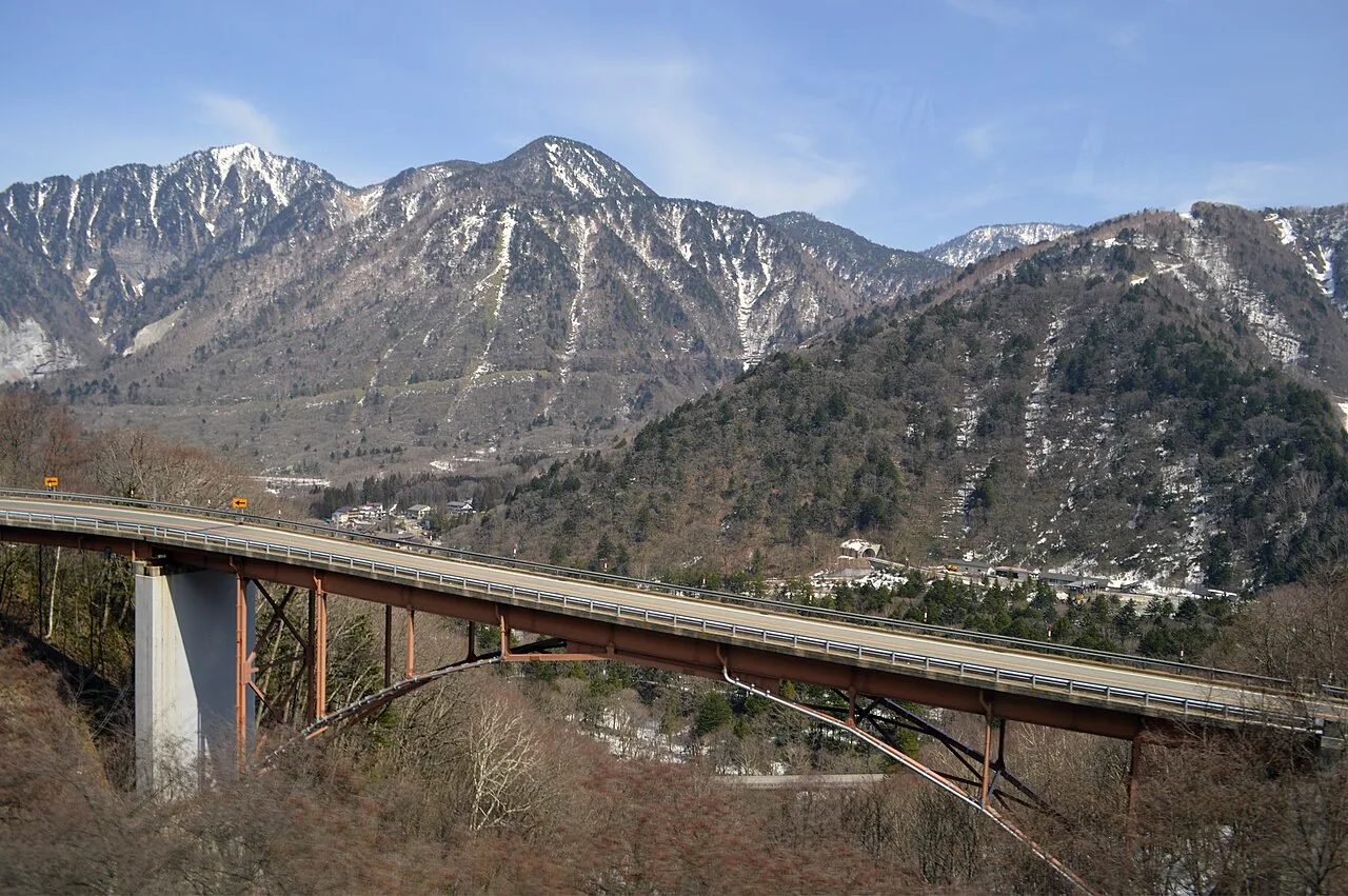 A road bridge on National Route 158 with snow-streaked Mount Akandana behind it in early spring