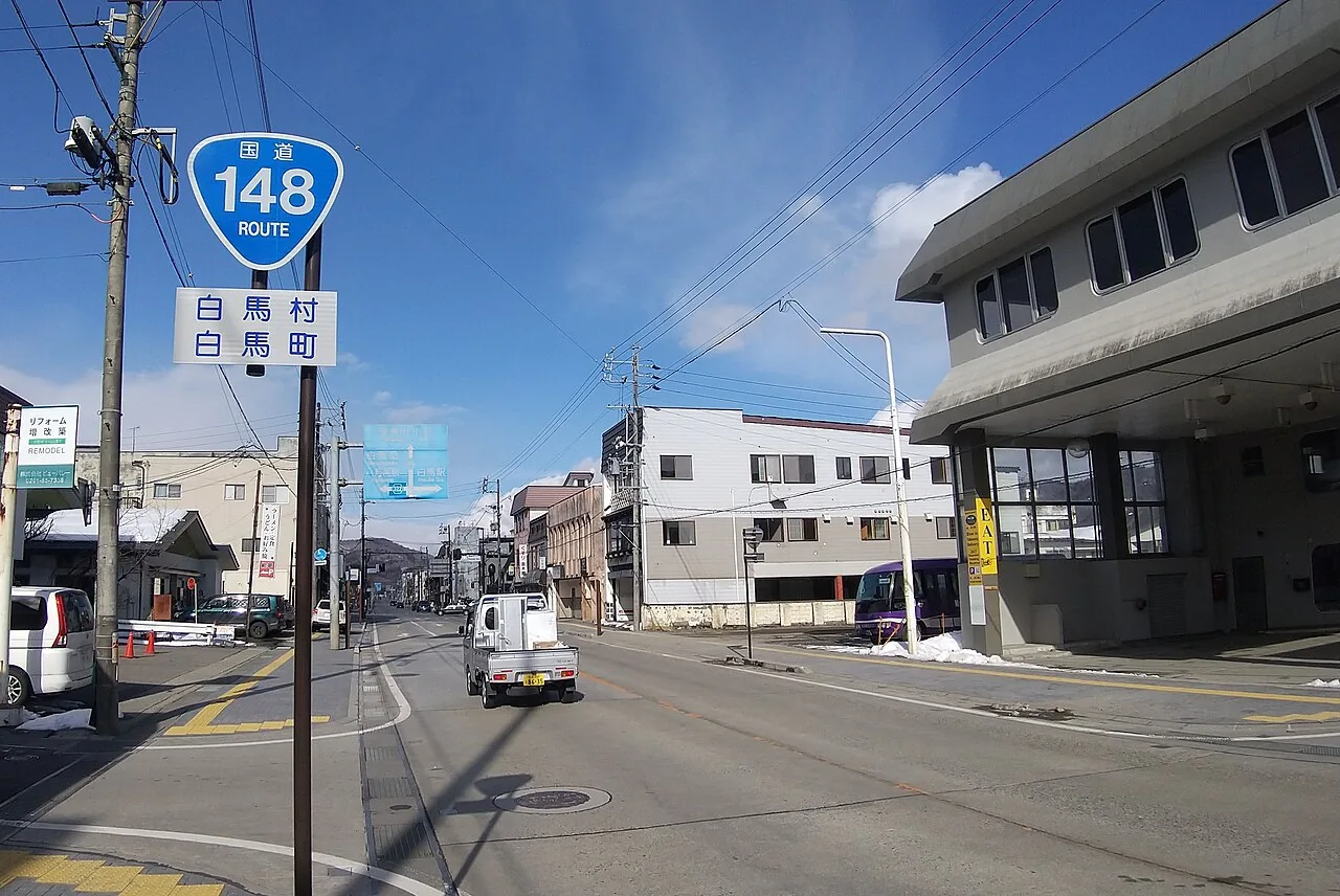 A Route 148 sign reading Hakuba Village on a sunny street, with snow left at the roadside